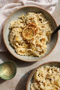 two bowls filled with macaroni and cheese on top of a table next to an orange slice