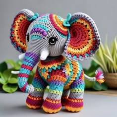 an elephant made out of crochet sitting on a table next to some plants