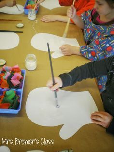 children are sitting at a table making paper cutouts