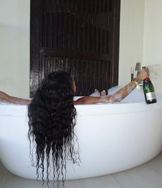 a woman with long hair sitting in a bathtub holding a bottle of booze