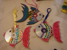 three colorful fish ornaments are hanging on a table with other decorations around them and one has a cd in the shape of a fish