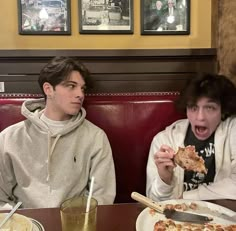 two people sitting at a table eating pizza and drinking soda, with one person holding a slice of pizza up to his mouth