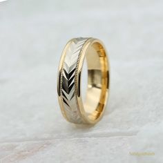 a wedding ring with an engraved design on the side and gold inlays, sitting on a white surface