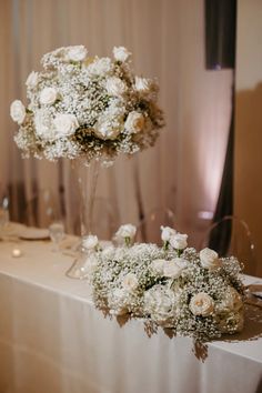 two tall vases filled with white flowers on top of a table