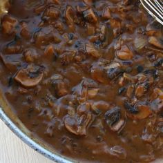 a pan filled with mushrooms and sauce on top of a wooden table