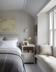 a bed sitting next to a window with white sheets and pillows on top of it