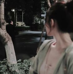 a woman standing in front of a tree at night with her back turned to the camera