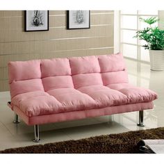 a pink futon sofa sitting on top of a white floor next to a potted plant