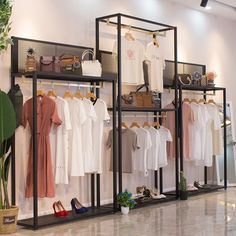 a clothing rack with clothes and shoes on it in a store or showroom next to a potted plant