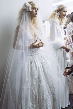 two women in wedding gowns standing next to each other with veils over their heads