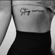 black and white photo of woman's back with tattoo saying stay curious