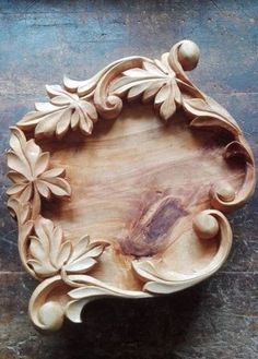 a wooden tray with flowers and leaves carved into the sides, on a wood surface