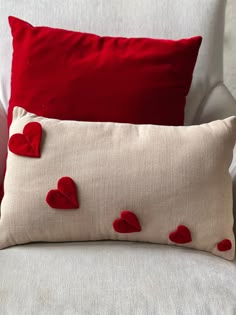 two pillows with hearts on them sitting on a couch next to each other, one red and the other white