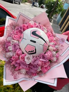 a bouquet of flowers and a soccer ball on top of pink paper in front of a red car