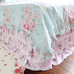 a bed with pink and blue floral bedspread on top of wooden flooring