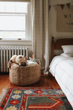 a basket filled with stuffed animals on top of a wooden floor next to a bed