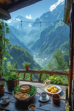 a wooden table topped with food on top of a lush green hillside covered in mountains