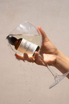 a hand holding a wine glass with a bottle in it and water pouring out of it