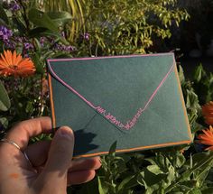 a hand holding an envelope with the word love written on it in front of some flowers