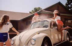 two girls in bathing suits washing a vw bug with water from a sprinkler