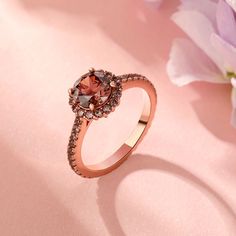 a pink diamond ring sitting on top of a pink surface next to purple and white flowers