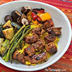 a white bowl filled with meat and veggies on top of a colorful table cloth