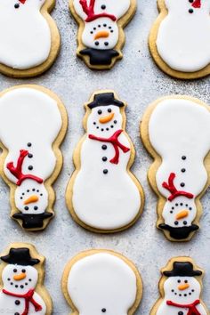 frosted cookies decorated like snowmen with hats and scarfs on them, lined up in rows