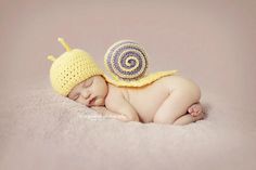 a baby wearing a crochet snail hat sleeping on top of a blanket next to a stuffed animal