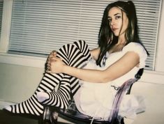 a woman sitting in a chair with her legs crossed, wearing striped stockings and tights