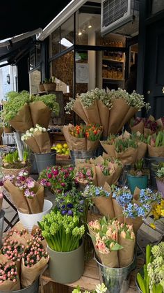 many different types of flowers in buckets on a table outside an outdoor market place