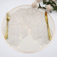 a white plate topped with two gold forks and a knife next to a bouquet of flowers