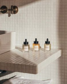 three bottles of body lotion sitting on top of a counter next to a sink