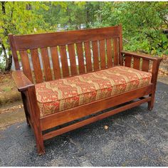 a wooden bench sitting on top of a cement ground next to some green trees and bushes