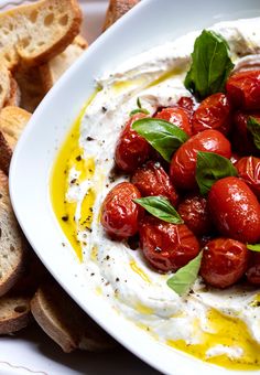 a white plate topped with bread and tomatos next to a bowl of sour cream