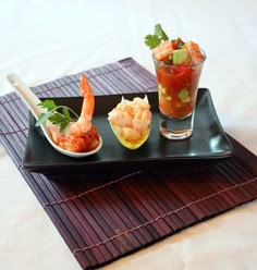 a black plate topped with shrimp and garnish next to a glass of water