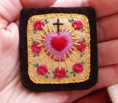 a hand holding a small embroidered cross and heart