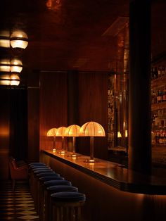 a dimly lit bar with several stools and lamps on the wall in front of it