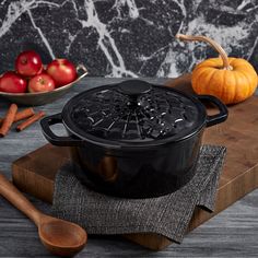 a large black pot sitting on top of a wooden cutting board next to apples and cinnamons