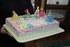 a person holding a birthday cake with candles on it in front of the cake is princess figures