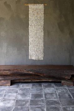 a wooden bench sitting on top of a tiled floor next to a wall with a woven curtain hanging above it