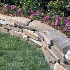 a stone bench sitting in the middle of a flower bed next to grass and flowers