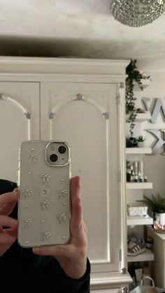 a person holding up a cell phone in front of a white cabinet and chandelier