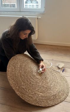 a woman sitting on the floor next to a large round rug with scissors in it