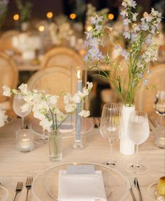 the table is set with white and blue flowers in glass vases, silverware, and wine glasses