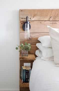 a bed with white sheets and pillows next to a wooden wall mounted shelf filled with books