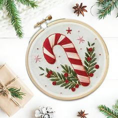 a cross stitch christmas candy cane on a white background surrounded by pine cones and other holiday decorations