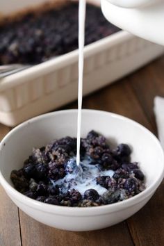 a bowl filled with blueberries and yogurt being poured into it