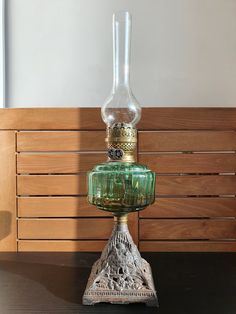 a green glass bottle sitting on top of a wooden table next to a lamp shade