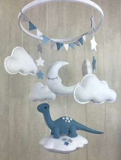 a baby mobile with a blue dinosaur on the moon and clouds hanging from it's side