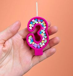 a hand holding a birthday candle shaped like the number 3 with sprinkles